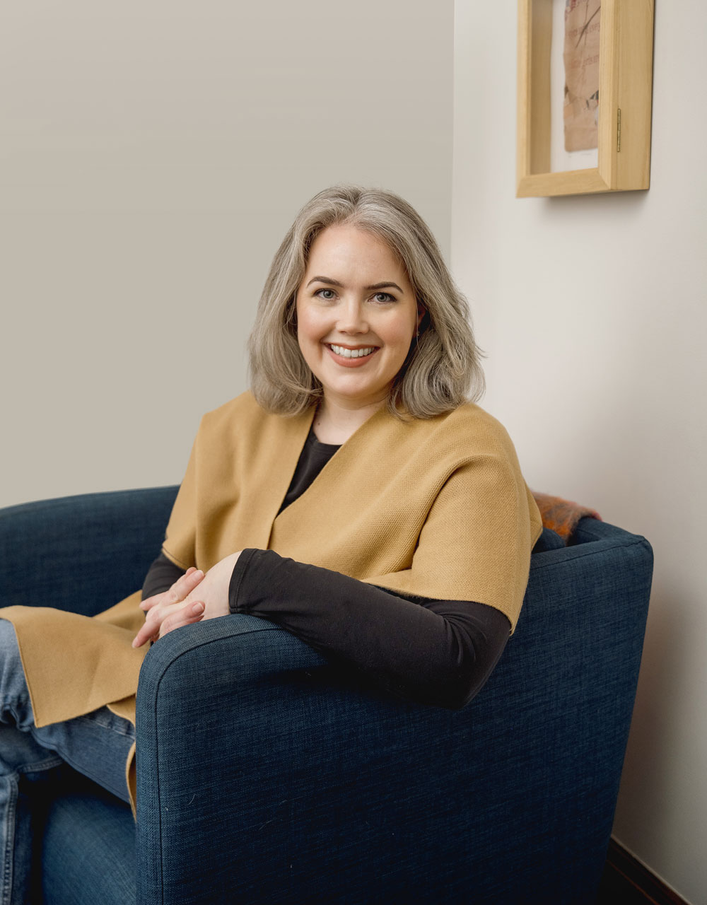 Katie Kamholz, ATR-BC, LCPC smiles and sits in a chair in her therapy office